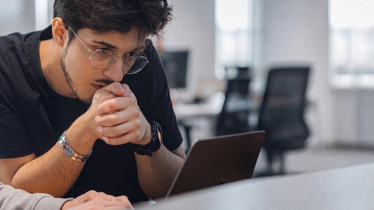 Una persona del team Yellow Tech, concentrata davanti al portatile, con l'ufficio sfocato sullo sfondo e le mani di un collega in primo piano