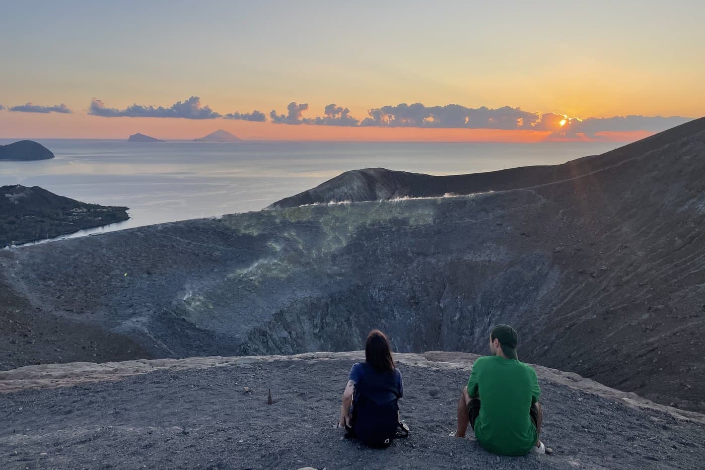 Due persone guardano il tramonto dal bordo di un cratere