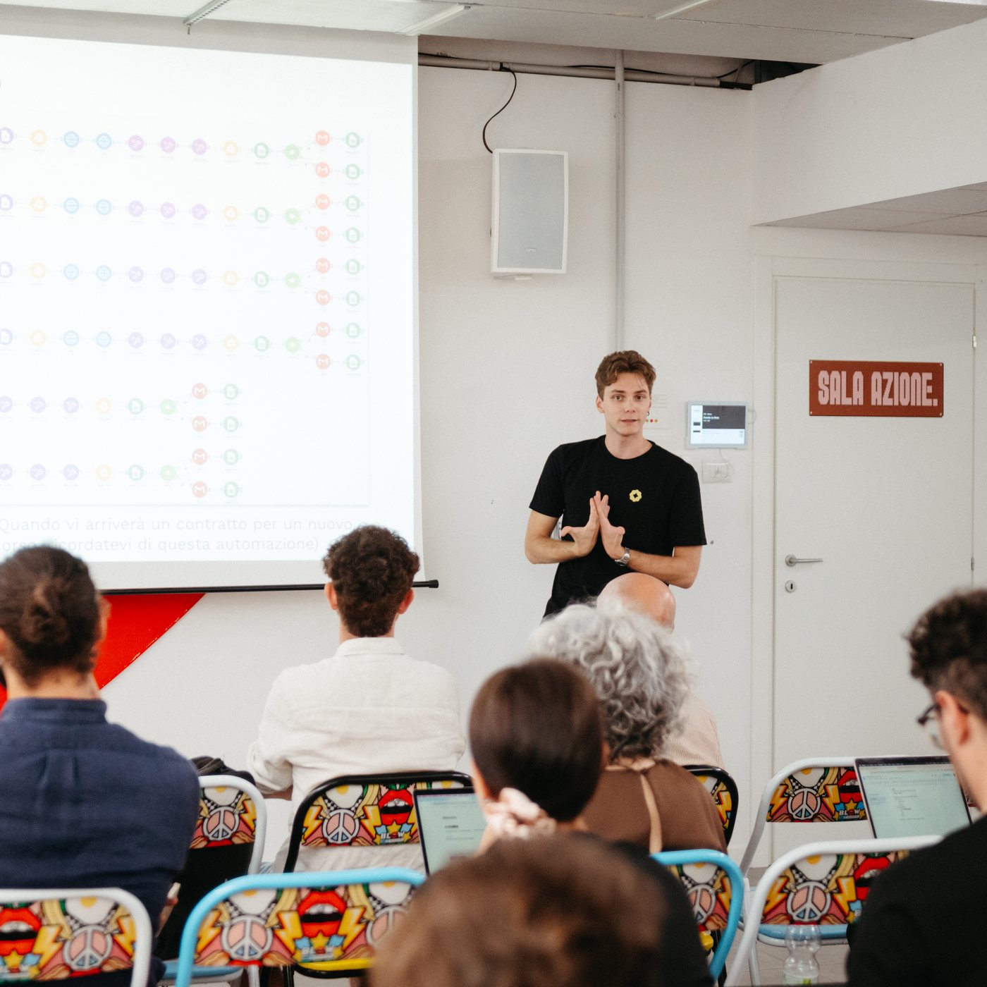 Una persona del team Yellow Tech presenta a una sala di partecipanti con i laptop aperti